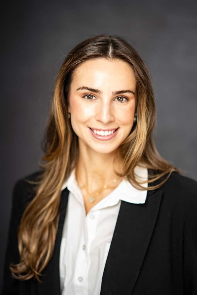Professional headshot of a woman with long hair, smiling in a black blazer and white blouse