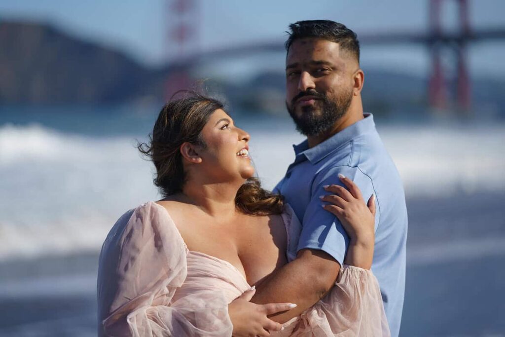 Couple embracing on Baker Beach with the Golden Gate Bridge in the background