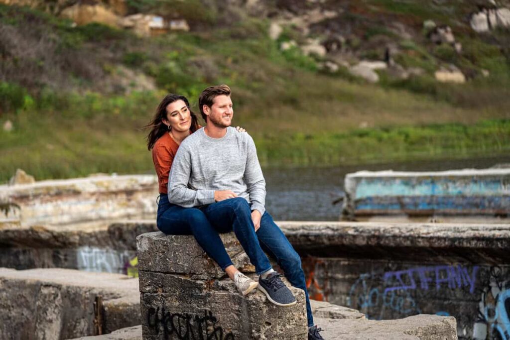Couple seated on a stone ledge at Sutro Baths in San Francisco, surrounded by nature
