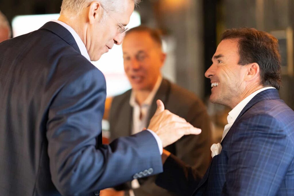 Corporate men smiling and shaking hands at an event photographed by Chris Conner