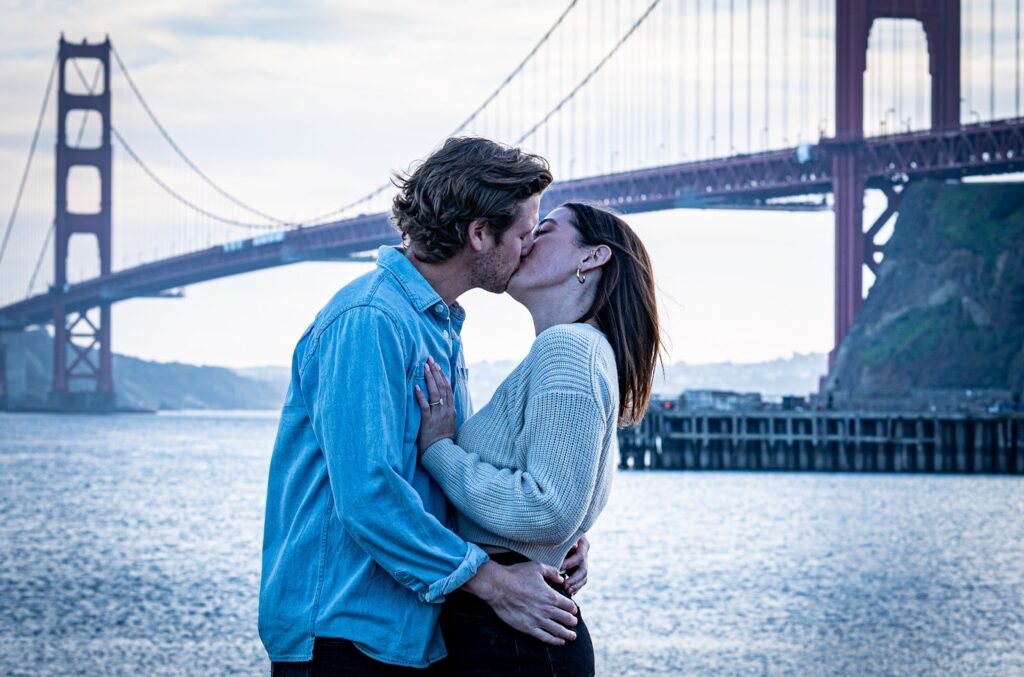 Couple kisses in front of the Golden Gate Bridge during an engagement session at Cavallo Point.