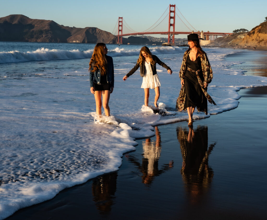 Three girls walking along the shoreline at sunset with the Golden Gate Bridge in the background at Crissy Field