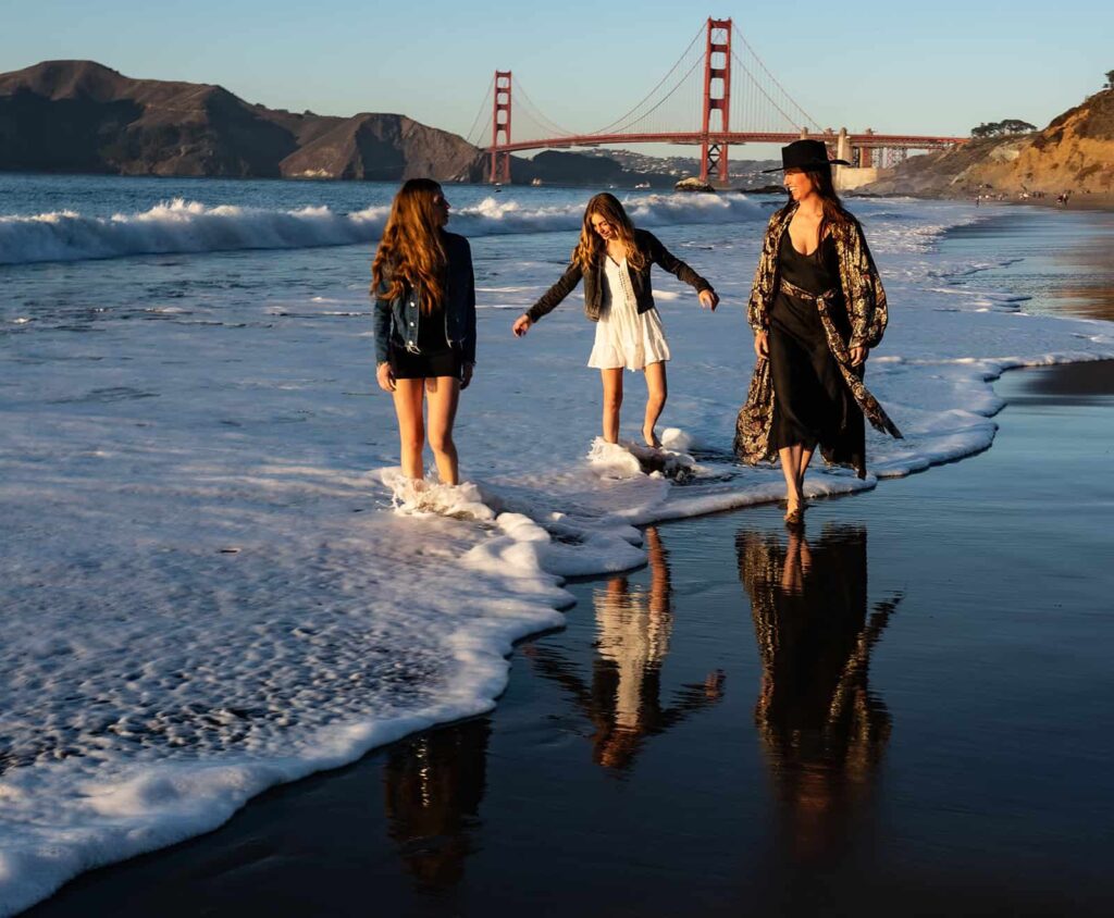 Family walking along the shore at Baker Beach with the Golden Gate Bridge in the background during sunset