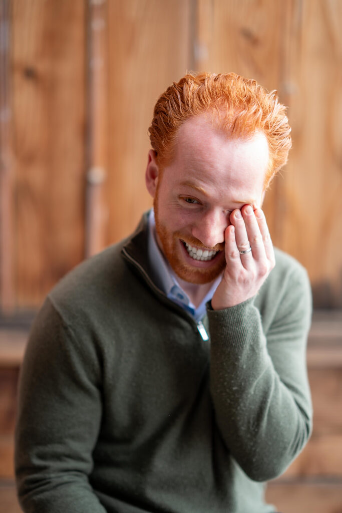 Man laughing with hand on face in front of wood background — candid professional headshot