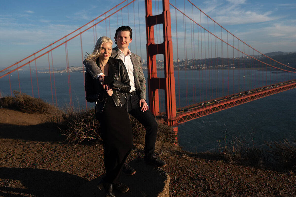 Couple posing on a rock overlooking the golden gate bridge at sunset