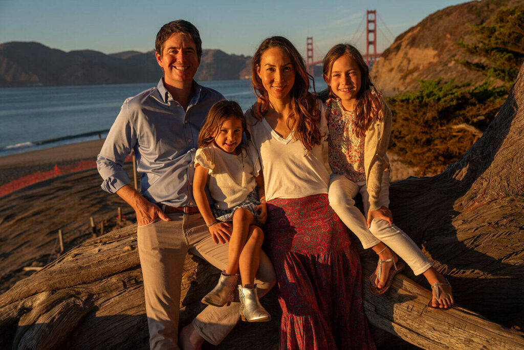 Family posing on the cliffs at Baker Beach with the Golden Gate Bridge in the background during golden hour