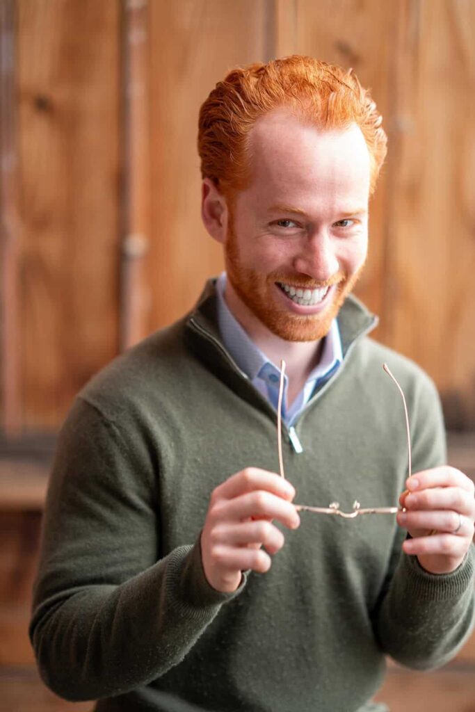 Professional headshot of a red-haired man holding eyeglasses and smiling, taken by Chris Conner Photography in San Francisco