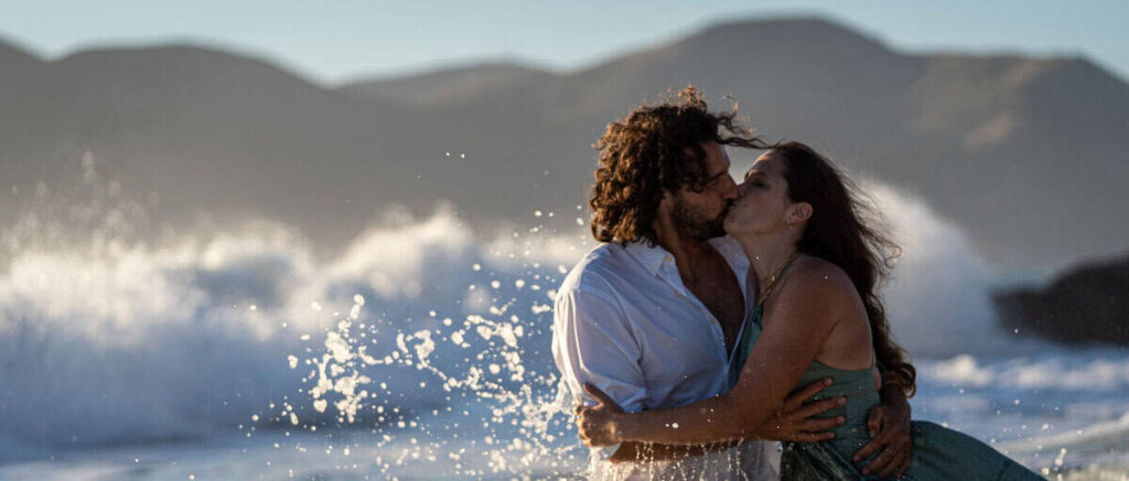 Couple embracing on the shoreline at Baker Beach during sunset with waves crashing behind them